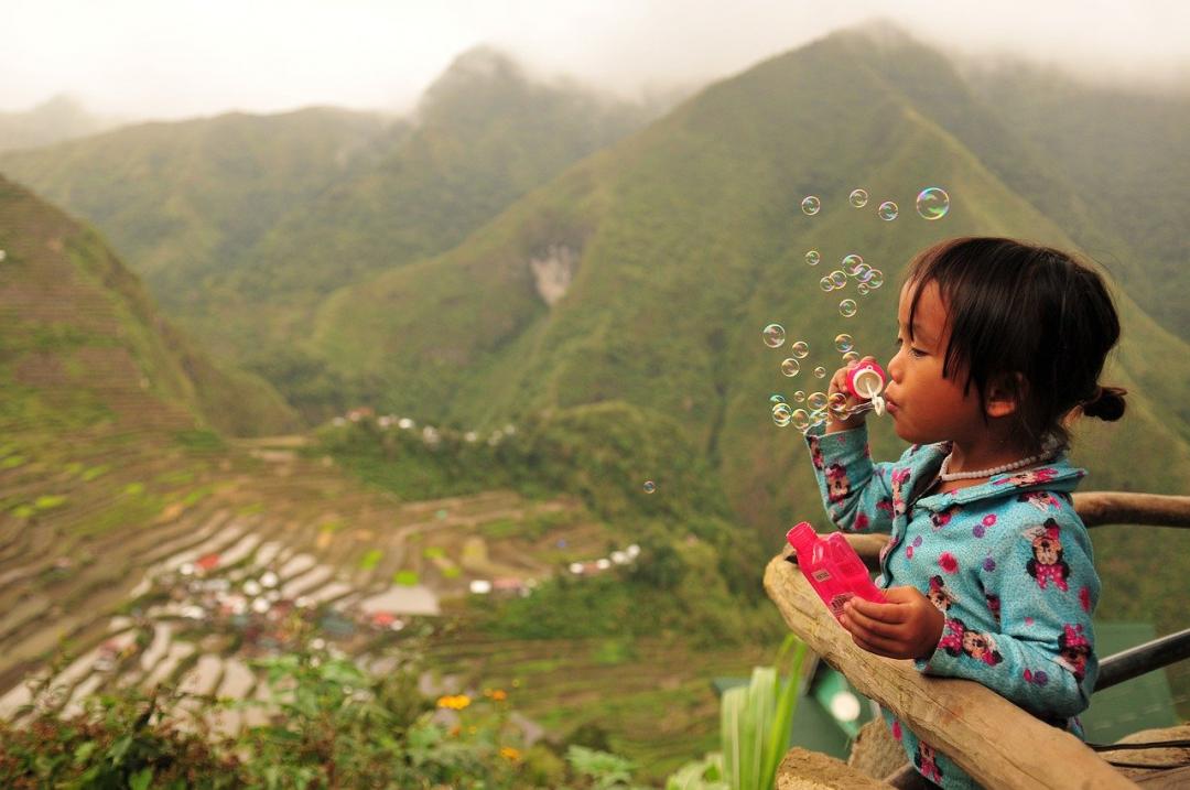 child blowing bubbles next to rice fields